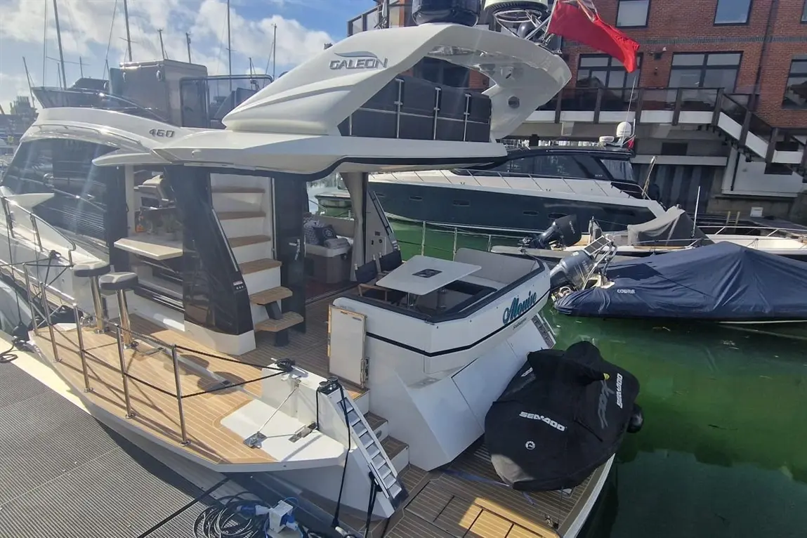 A sleek Galeon 460 yacht docked at a marina, featuring stairs, seating area, and luxury finishes, with visible luxury boats nearby.